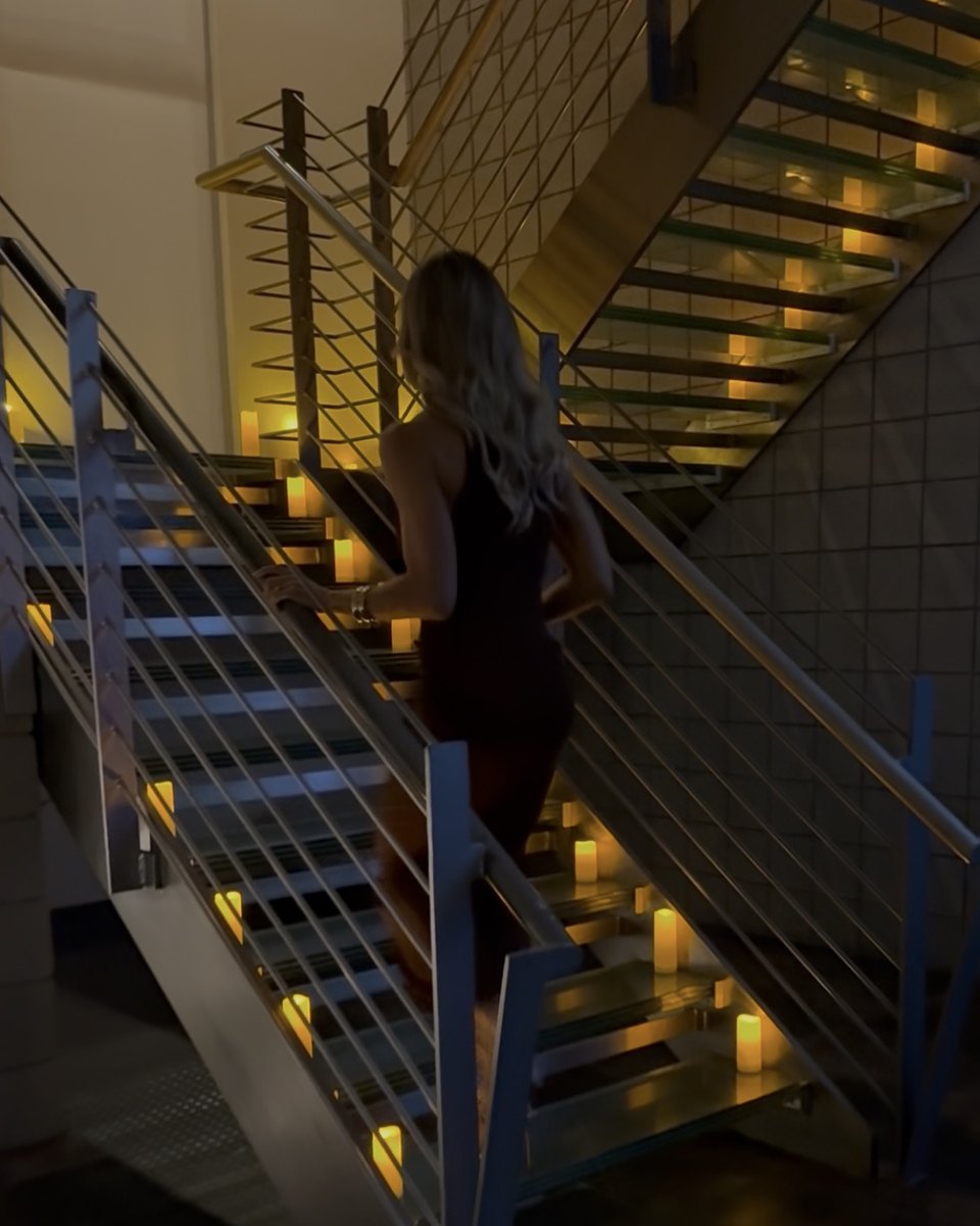 A woman in a black dress climbing a staircase lined with candles
