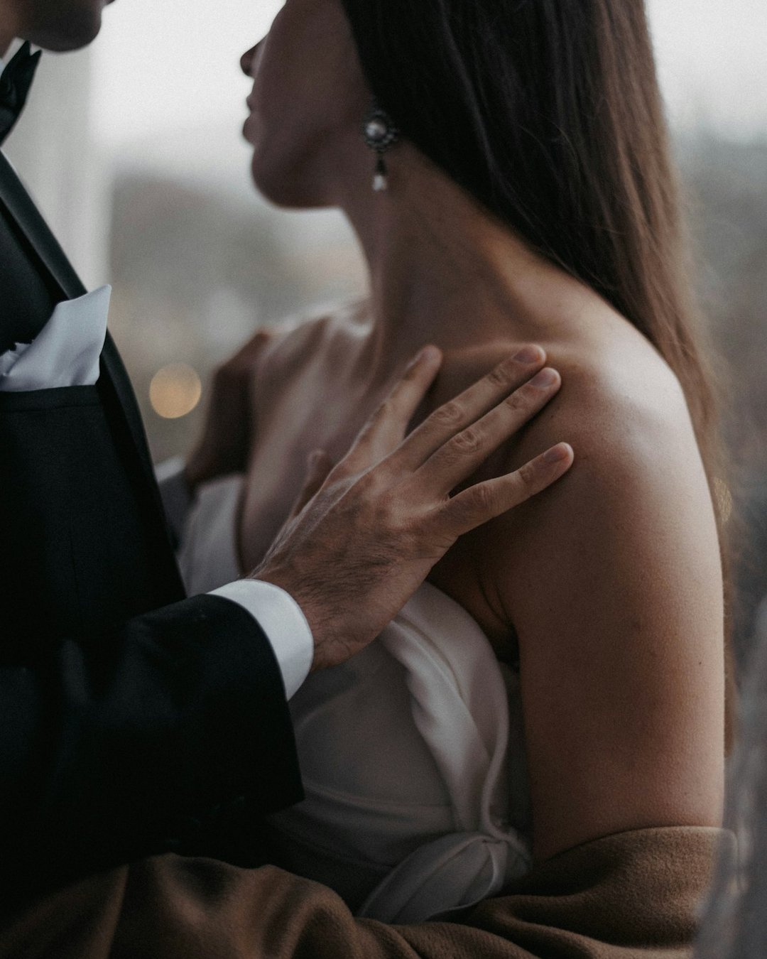 A man in a tuxedo with his hand on the bare shoulder of a woman in a white gown